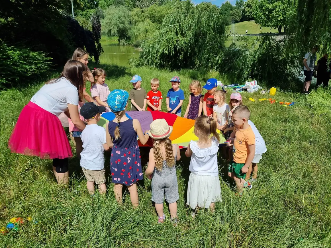 Animatorka prowadzi dużą grupę dzieci podczas zabawy z kolorową chustą