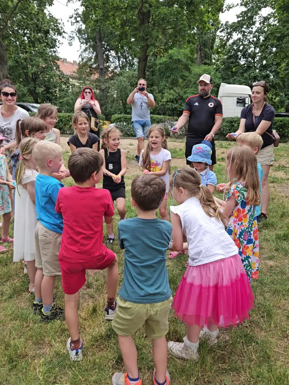 Animatorka tłumaczy zasady zabawy grupie dzieci na świeżym powietrzu