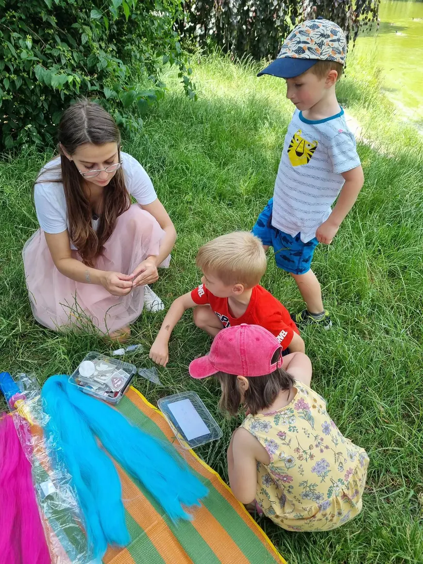 Animatorka pokazuje dzieciom kolorowe akcesoria podczas zabawy w plenerze