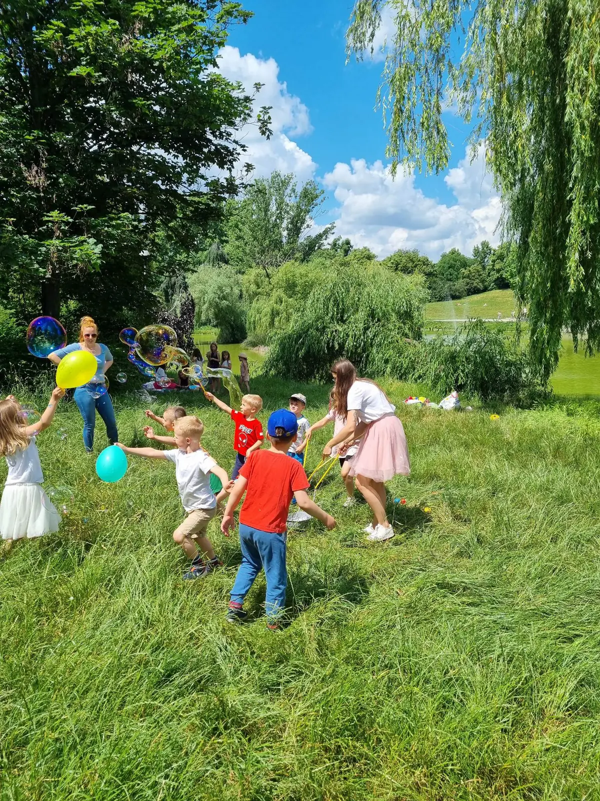 Dzieci i animatorka bawiacy sie bankami mydlanymi na trawie